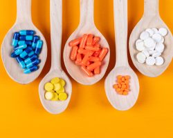 Top view colorful pills in wooden spoons on orange background. horizontal