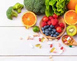 A top view of fresh fruits and vegetables with different medicine on a wooden spoon